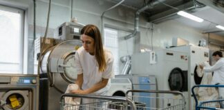 Pracownicy obsługują duże pralki i suszarki w pralni przemysłowej