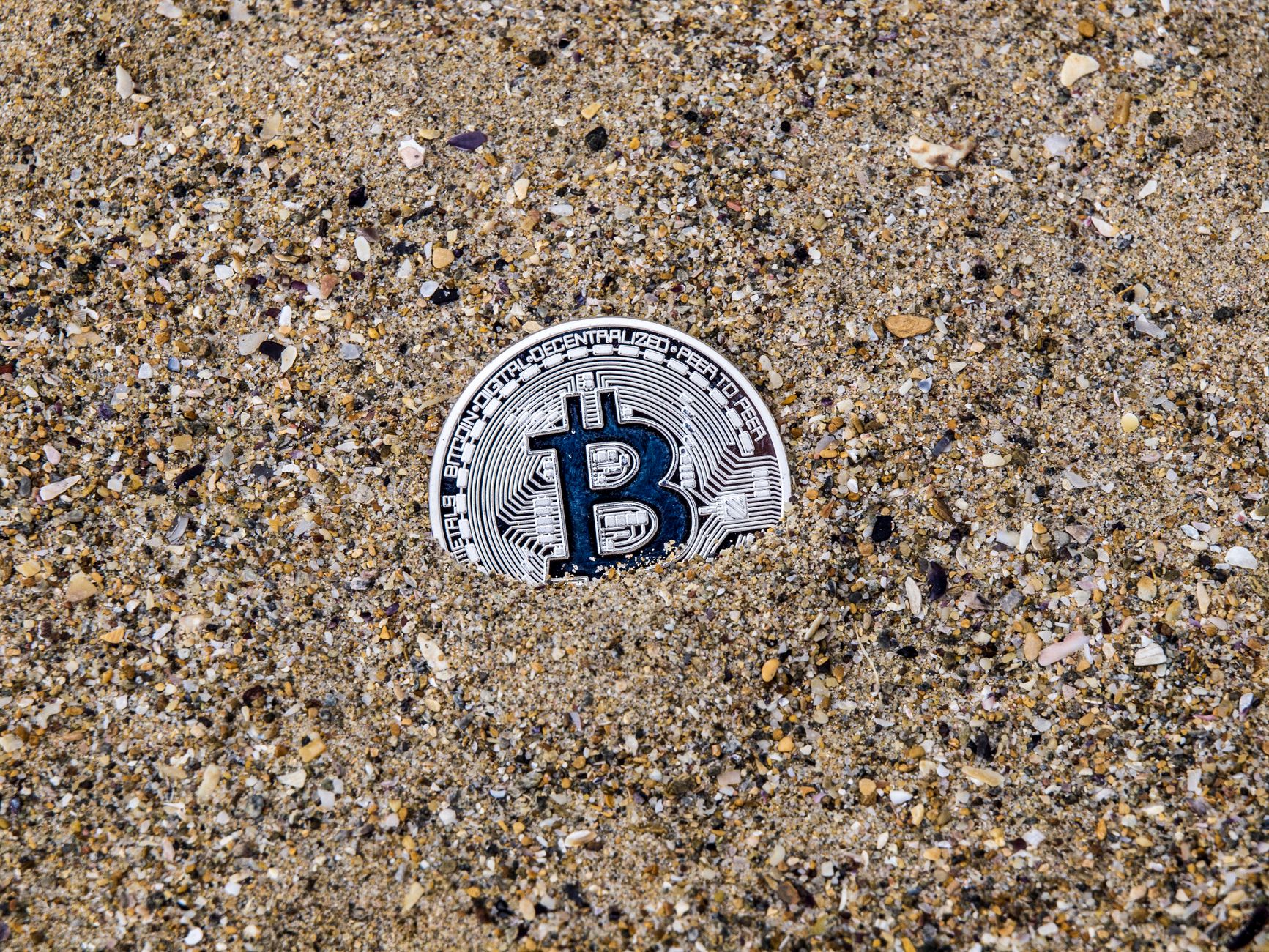 Symbol Bitcoina częściowo zakopany w piasku