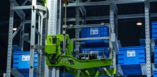 Zielone ramię robota przenoszące niebieskie pojemniki w automatycznym magazynie