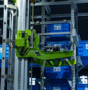 Zielone ramię robota przenoszące niebieskie pojemniki w automatycznym magazynie