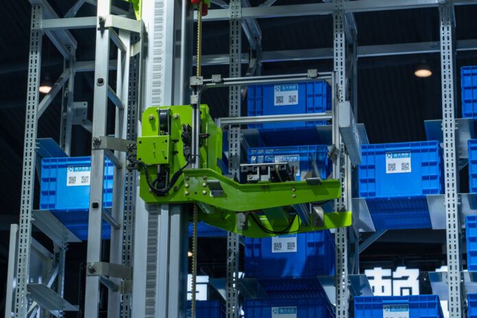 Zielone ramię robota przenoszące niebieskie pojemniki w automatycznym magazynie Zielone ramię robota przenoszące niebieskie pojemniki w automatycznym magazynie